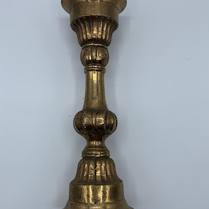 May include: A gold metal candlestick with an ornate design. The candlestick has a wide base and a tall, slender stem.