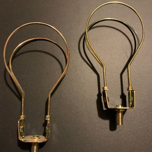 May include: Two gold metal light bulb cage holders. Each holder has a threaded base and a circular cage that surrounds the bulb.