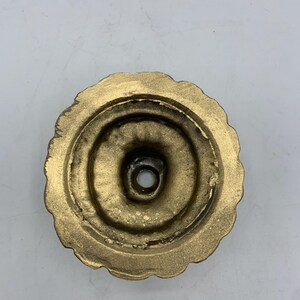 May include: A gold-colored, circular decorative object with a scalloped edge. The center has a hole, and the piece has a textured appearance. The object appears to be made of metal.