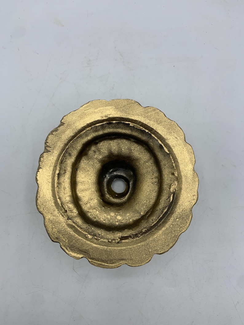 May include: A gold-colored, circular decorative object with a scalloped edge. The center has a hole, and the piece has a textured appearance. The object appears to be made of metal.