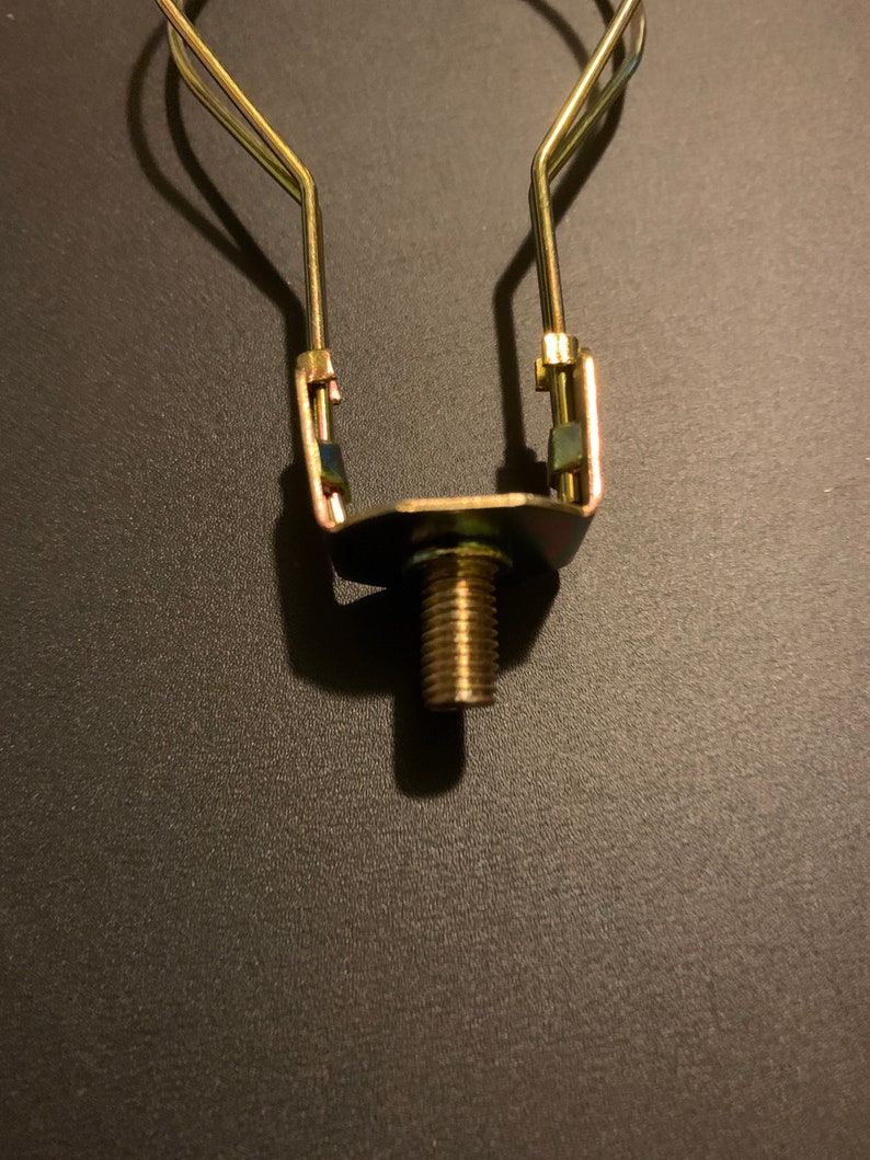 May include: A gold metal lamp harp with a threaded screw for attaching a lampshade.