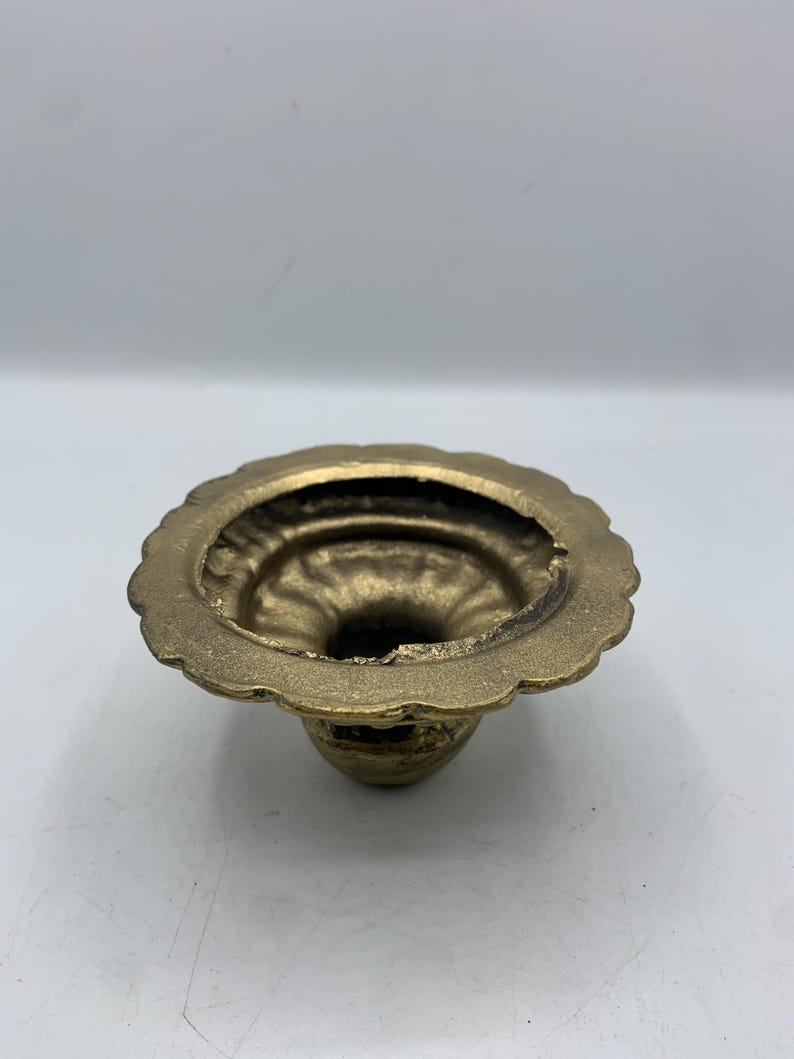 May include: A small, antique brass candle holder with a scalloped rim. The candle holder has a round base and a flared opening. The brass has a warm, golden hue and shows signs of age.