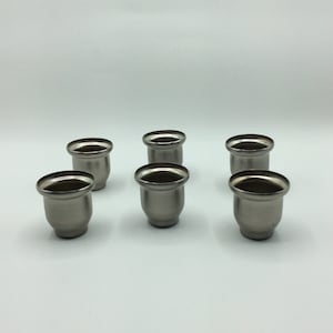 May include: Six silver candle holders, each with a round, slightly flared base and a smooth, polished finish.