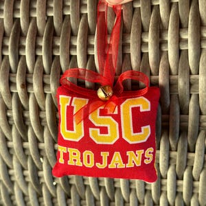 May include: Red and yellow fabric ornament with a bell and the words "USC Trojans" on it.