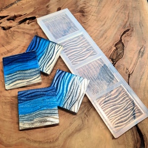 May include: A set of six clear silicone molds for making resin coasters. The molds are arranged in a row on a wooden surface. Each mold has a different design, featuring a wavy pattern.