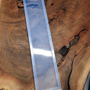 May include: A clear rectangular silicone mould for resin casting. The mould is sitting on a wooden surface.