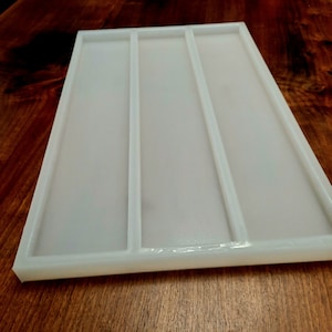 May include: White silicone mold with three long rectangular cavities. The mold is designed for creating resin crafts.