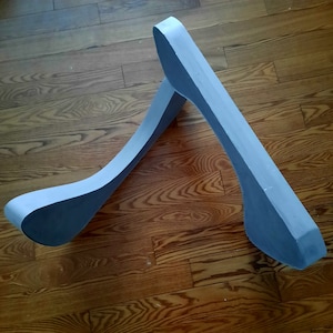 Op de afbeelding: Een lichtgrijze schuimvorm die lijkt op de letter A, met een gebogen bovenkant en een afgeronde basis. De vorm ligt op een houten oppervlak.