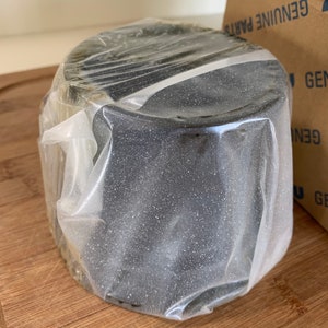 Pu&ograve; includere: Un oggetto rotondo nero avvolto in plastica trasparente. L'oggetto &egrave; su una superficie di legno.