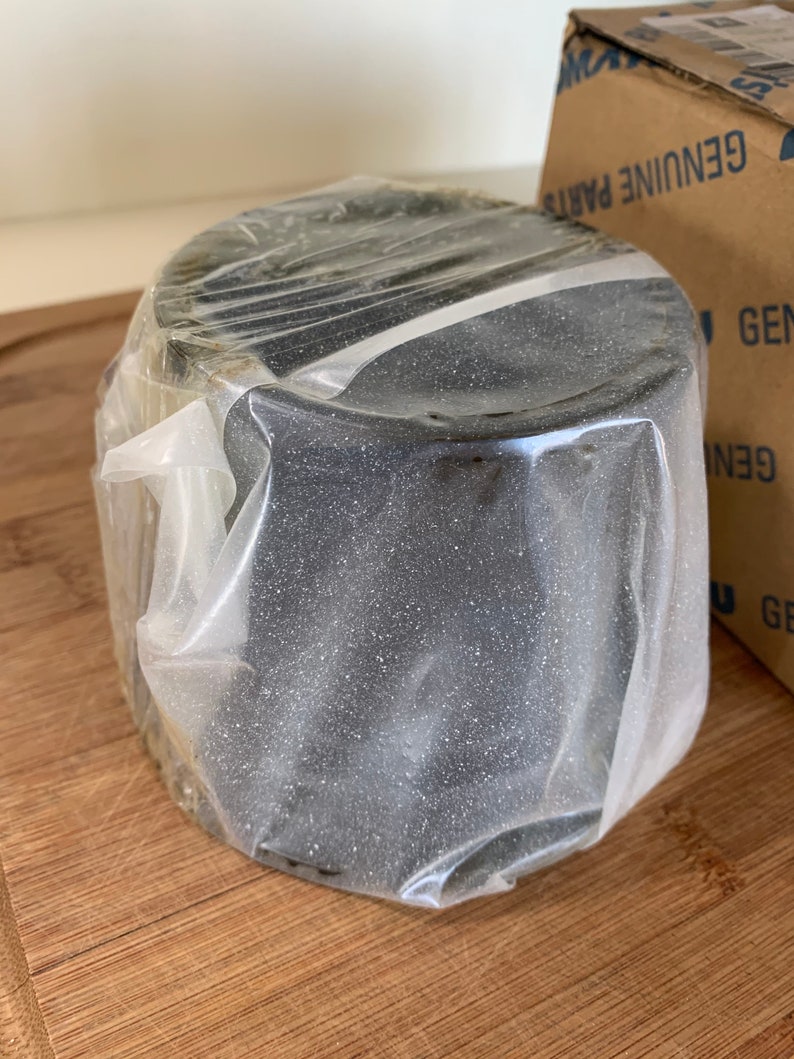 Pu&ograve; includere: Un oggetto rotondo nero avvolto in plastica trasparente. L'oggetto &egrave; su una superficie di legno.