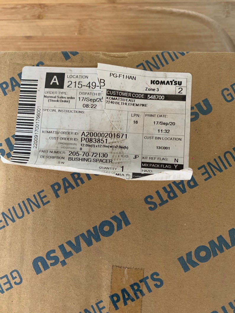 Pu&ograve; includere: Una scatola di cartone marrone con un'etichetta bianca che dice "KOMATSU" e contiene le seguenti informazioni d'ordine: "A 215-49-B", "CODICE CLIENTE: 548700", "NUMERO D'ORDINE KOMATSU: A20000201671", "NUMERO D'ORDINE CLIENTE: P083851", "NUMERO PEZZO: 205-70-72130", "DESCRIZIONE: DISTANZIALE", "QUANTIT&Agrave;: 1".