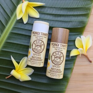 Könnte beinhalten: Zwei zylindrische Deodorant-Sticks mit der Aufschrift Monoi Tahiti with Gardenia Tiare Tiki Flower und Kokoa Botanics Sport Natural Deodorant. Ein Stick hat eine weiße Kappe, der andere eine Kappe in Holzoptik. Beide geben 90g Nettogewicht an.