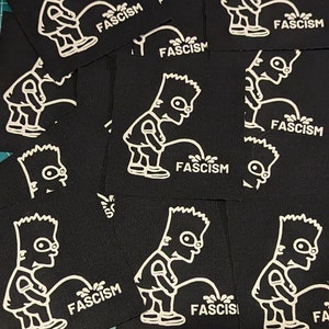 May include: A collection of black fabric patches featuring a white cartoon figure urinating on the word "FASCISM". The patches are square and have a white outline of the cartoon character and text.