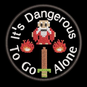 May include: A black and white embroidered patch with a red and white pixelated character holding a sword. The text around the character reads "It's Dangerous To Go Alone".