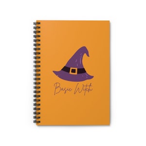 May include: A spiral bound notebook with an orange cover featuring a purple witch's hat with a black buckle and the text "Basic Witch" in purple.