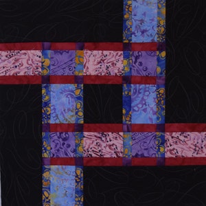 May include: A quilt block with a black background and a grid pattern of red, blue, and purple fabric squares. The fabric squares have a paisley design.