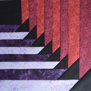 May include: A quilt block with a geometric pattern of black, purple, and red fabric. The fabric has a floral pattern.