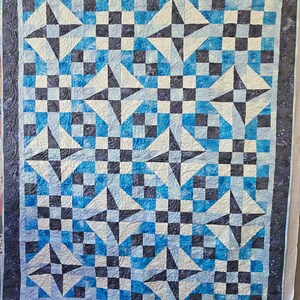 May include: A quilt with a blue, white and black chequered pattern. The quilt is made up of a series of triangles that create a star-like design.