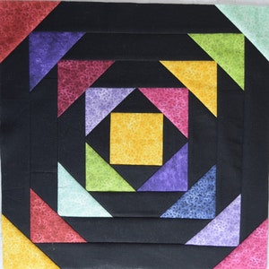 Pode incluir: Um bloco de colcha colorido com um quadrado amarelo central rodeado por várias formas geométricas. O design incorpora triângulos e quadrados em tons de roxo, rosa, verde e vermelho, sobre um fundo preto. O tecido tem uma textura estampada.