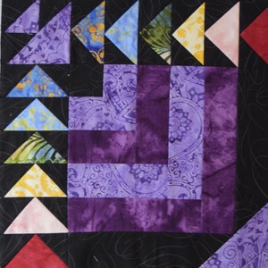 May include: A quilt block with a purple and black design. The block is made up of several smaller squares and triangles. The triangles are in various colors, including blue, green, yellow, pink, and red.
