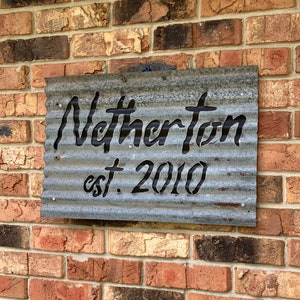 May include: A corrugated metal sign with the name "Netherton" cut out in a bold, black font, with "est. 2010" below. The sign is mounted on a brick wall, showcasing a rustic, industrial aesthetic.