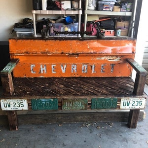 May include: A rustic wooden bench with a bright orange metal top. The bench is decorated with vintage license plates that read "UW-235" and "KE-7042". The metal top has the word "CHEVROLET" printed on it.