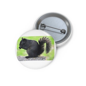 May include: A black squirrel sits on a log, eating a nut. The squirrel has a bushy tail and bright eyes. The background is a blurry green.
