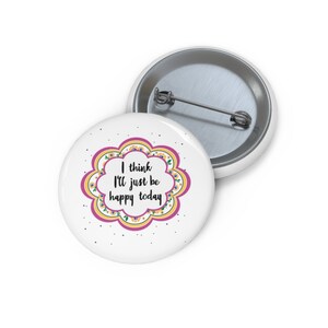 May include: White button with a pink and yellow floral design. The text "I think I'll just be happy today" is written in black.