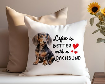 Puede incluir: Almohada blanca con una ilustración de un dachshund negro y marrón y el texto "Life is better with a dachshund" con tres corazones rojos.