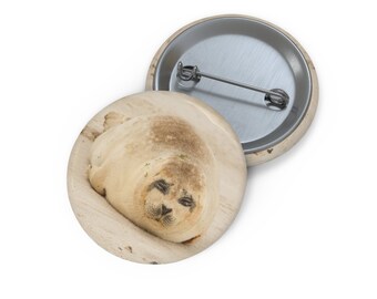 May include: A close-up of a seal lying on a sandy beach. The seal has its eyes closed and its mouth slightly open. The seal is light brown in color with a white belly.