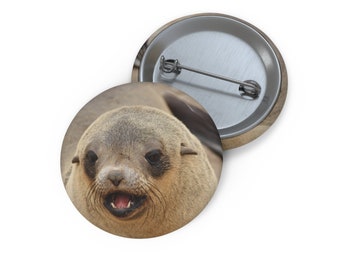May include: Close-up of a brown and gray seal with its mouth open, showing its teeth. The seal has dark eyes and a wet nose. The background is blurred and out of focus.