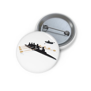 May include: A white button featuring a black silhouette of a rowing team in a boat with oars. The team is in the foreground and a single rower in a boat is in the background.