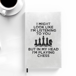 May include: White notebook with a black chessboard design and the text "I might look like I'm listening to you but in my head I'm playing chess".