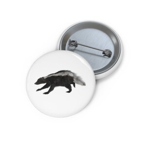 May include: A white button with a black and white skunk running to the right. The skunk has a white stripe down its back.