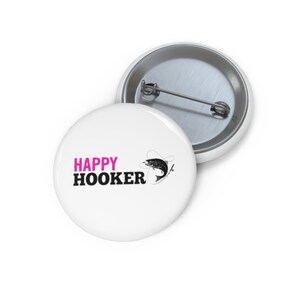 May include: White button with black text that says "HAPPY HOOKER" in pink. A black and white illustration of a fish on a hook is to the right of the text.