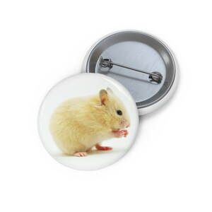 May include: A small, light yellow hamster sits on a white background and is eating. The hamster has a fluffy coat and small pink ears.