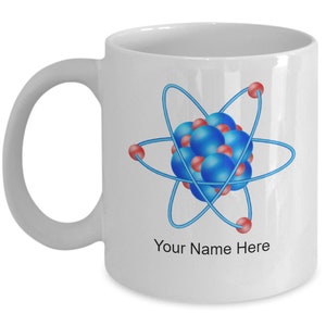 以下が含まれることがあります： 白いセラミック製のマグカップ。青と赤の原子イラストと「Your Name Here」という文字が前面に印刷されています。