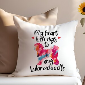 May include: White throw pillow with the text "My heart belongs to my labradoodle" in black lettering. A colorful abstract painting of a labradoodle is in the center of the pillow.