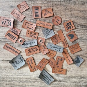 Könnte beinhalten: Eine Sammlung brauner Papieretiketten mit schwarzem Text. Die Etiketten zeigen verschiedene Phrasen und Wörter, darunter "Cool Socke", "Einzig Artig", "Selbst Gemacht", "Queen of All Toys" und "Holla hein!"