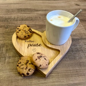Könnte beinhalten: Ein herzförmiges Holztablett mit einer weißen Tasse und Schokoladenkeksen. Das Tablett trägt den Text "Kaffee-pause" und ein Herz ist eingraviert.
