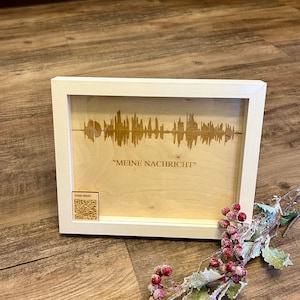 Könnte beinhalten: Eine weiße gerahmte Holzplakette mit einem Schallwellendesign und dem Text "MEINE NACHRICHT" in einem weißen Rahmen. Ein QR-Code befindet sich in der linken unteren Ecke mit dem Text "Scan mich."