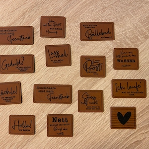 Könnte beinhalten: Eine Sammlung von 12 braunen Lederuntersetzern mit verschiedenen Sprüchen in Schwarz gedruckt. Die Sprüche lauten: "Katzenhaare sind mein Feenstaub", "Geduld?", "Lächle!", "Jeder hat das Recht auf meine Meinung", "Lass mal", "Hundehaare sind mein Feenstaub", "Kann mir bitte jemand ein Bällebad einräumen?", "Stress hilft nicht", "Nett könnte ich auch! Bringt aber nichts", "Kann mir bitte jemand das Wasser reichen", "Ich laufe *weil ich Schokolade liebe*" and "Holla! die Waldfee".