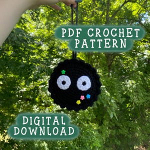 Könnte beinhalten: Ein schwarzer gehäkelter Charakter mit weißen Augen und bunten Akzenten. Das Bild enthält den Text "PDF Crochet Pattern" und "Digital Download". Der Charakter hängt vor einem Hintergrund aus grünem Laub.