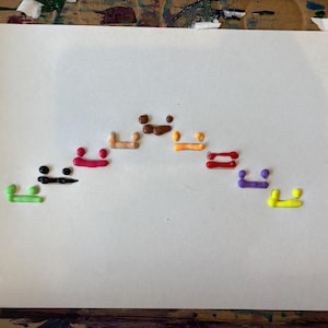 May include: A white sheet of paper with a rainbow of paint colours in the shape of an arch. The colours are green, black, pink, orange, red, purple, and yellow.