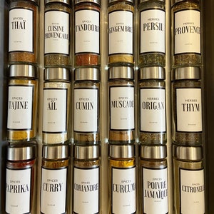 Peut inclure: Un ensemble de 18 bocaux à épices en verre avec des couvercles argentés et des étiquettes blanches. Les étiquettes comportent du texte noir et listent diverses épices et herbes en français, notamment Thai, Provençale, Tandoori, Gingembre, Persil, Provence, Tajine, Ail, Cumin, Muscade, Origan, Thym, Paprika, Curry, Coriandre, Curcuma, Poivre Jamaïcain et Citronnelle.