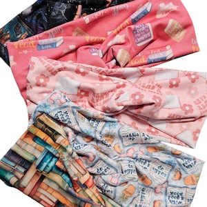May include: A collection of five fabric headbands with various patterns. Designs include books, flowers, and celestial themes. Colors range from pink and blue to a vibrant stack of books.