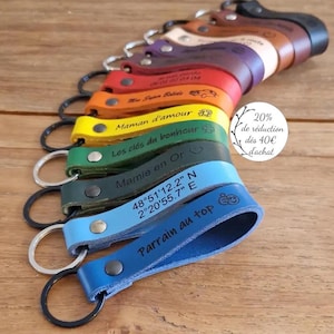 May include: A collection of leather keychains in various colors, each with a metal ring and a snap closure. The keychains are engraved with phrases and coordinates. The text "Parrain au top" is visible on a blue keychain.