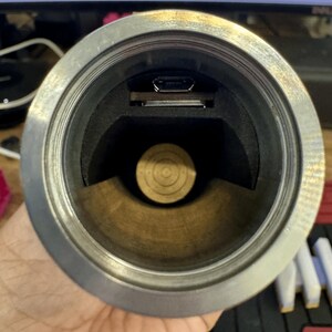 May include: Close-up view of the inside of a silver metal tube with a black foam lining. A small black USB port is visible in the top of the tube.