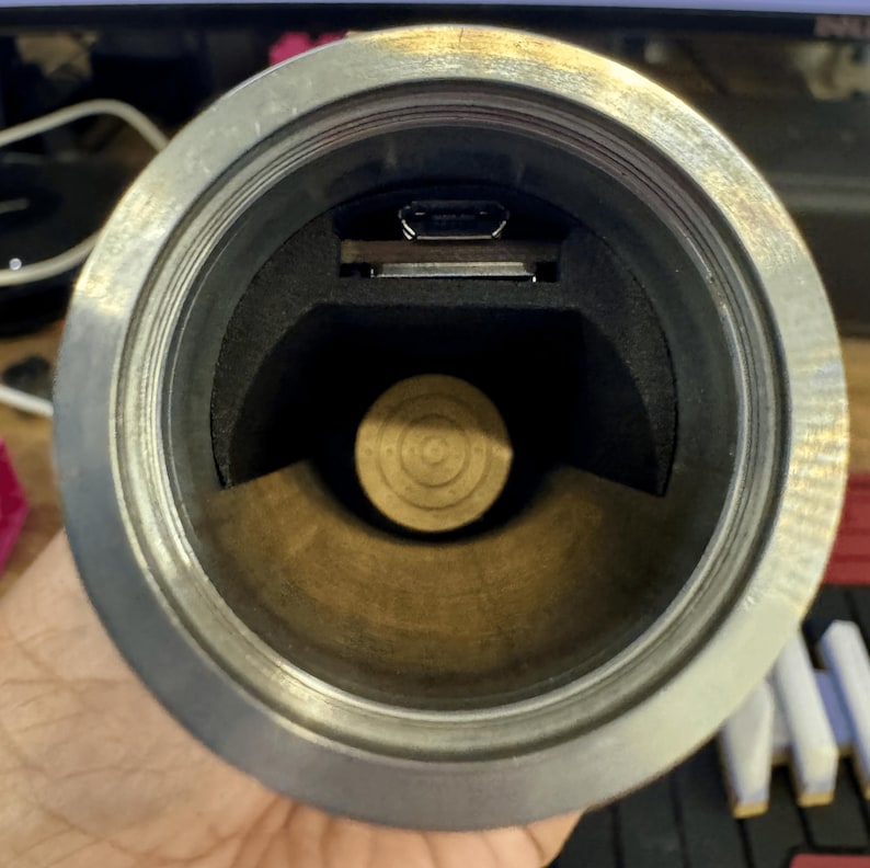 May include: Close-up view of the inside of a silver metal tube with a black foam lining. A small black USB port is visible in the top of the tube.