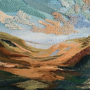 K&ouml;nnte beinhalten: Eine Wandteppich, der eine Landschaft mit blauem Himmel und flauschigen wei&szlig;en Wolken darstellt. Der untere Teil des Wandteppichs zeigt ein Tal mit braunen und gr&uuml;nen H&uuml;geln.